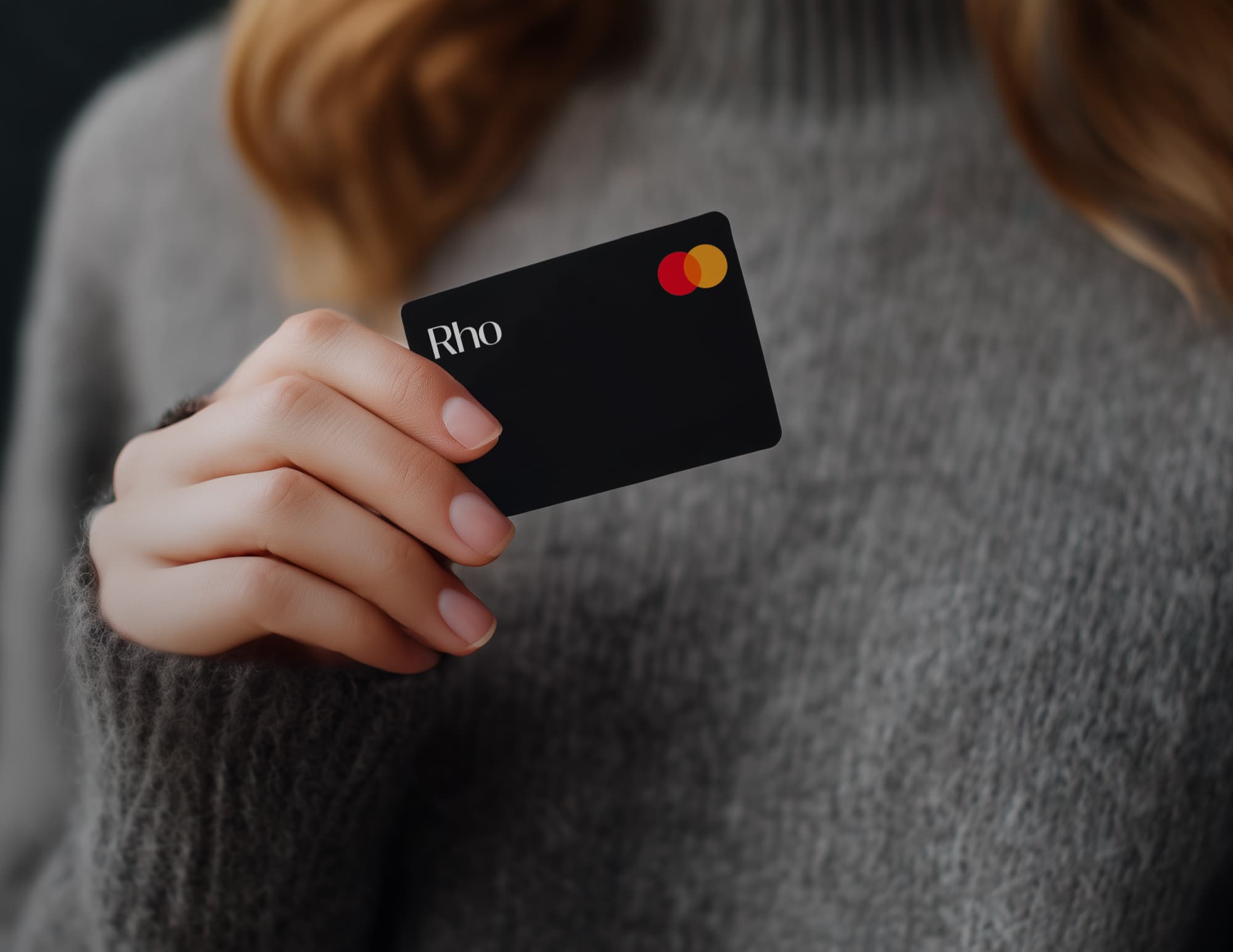 Woman in gray sweater holding Rho credit card